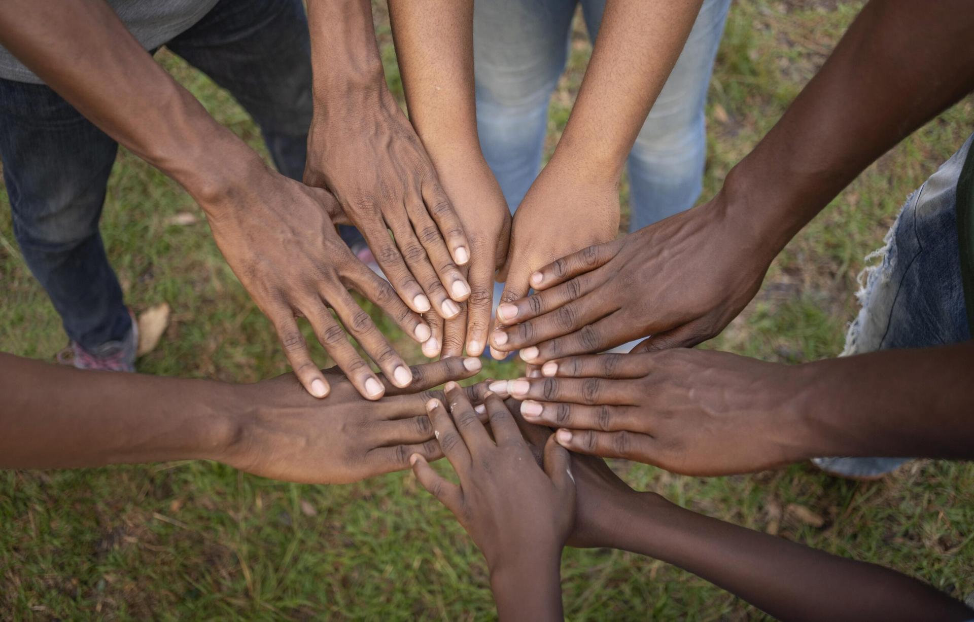Young people of African descent joining hands in a circle on grass